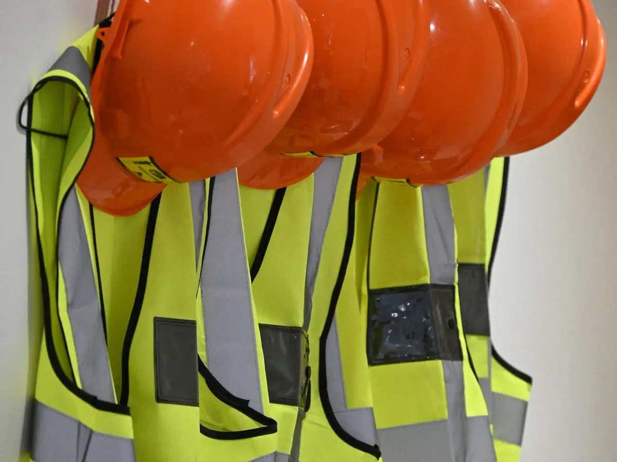 Orange hard hats and yellow high-visibility vests hanging on hooks
