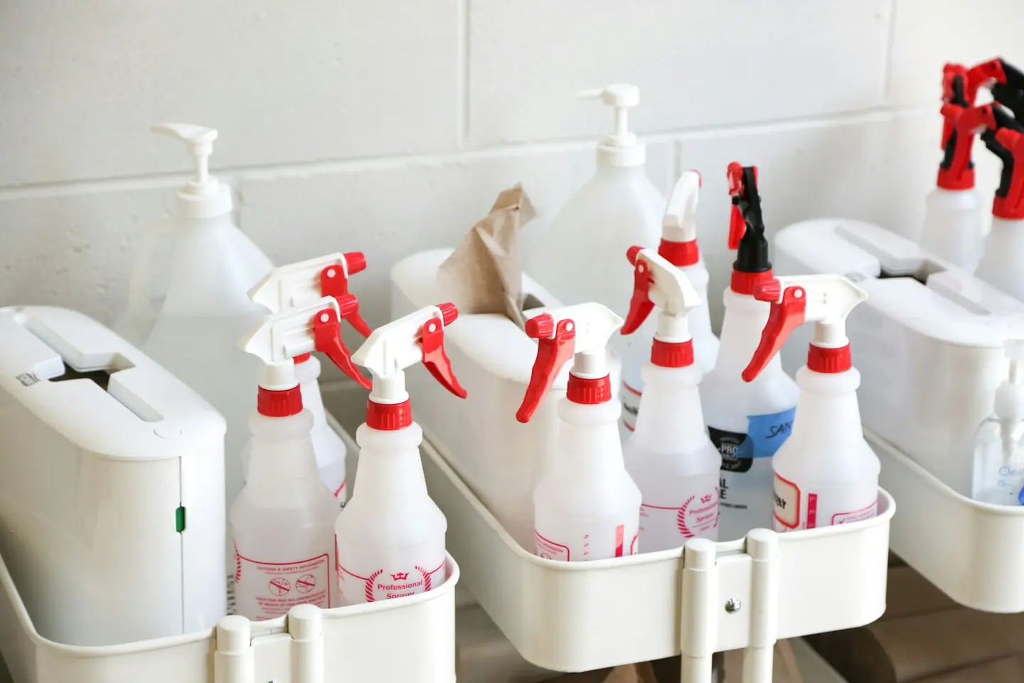 Rows of spray bottles and gallon jugs of cleaning products in plastic caddies